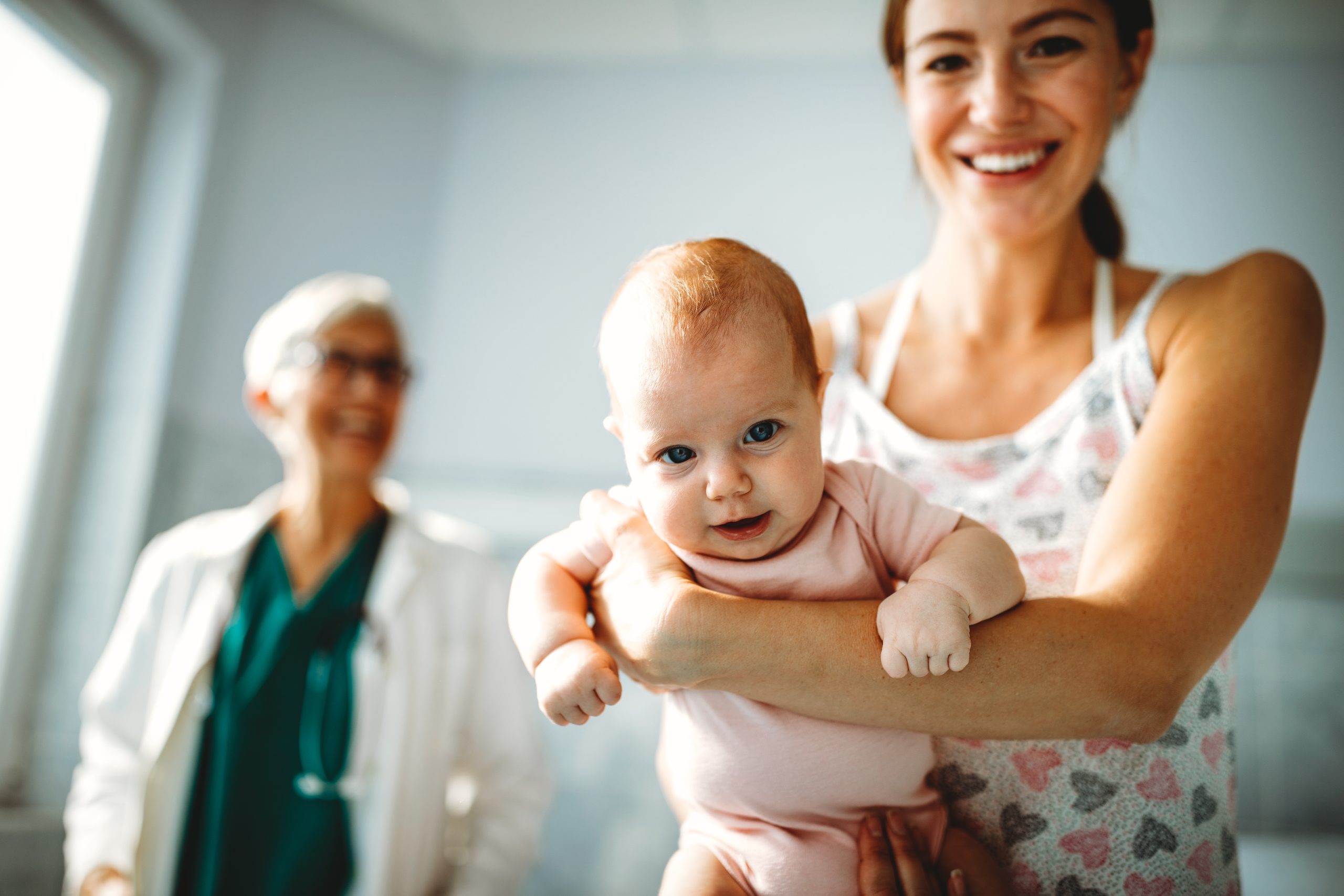 mom holding baby at doctor's office with doctor in the background