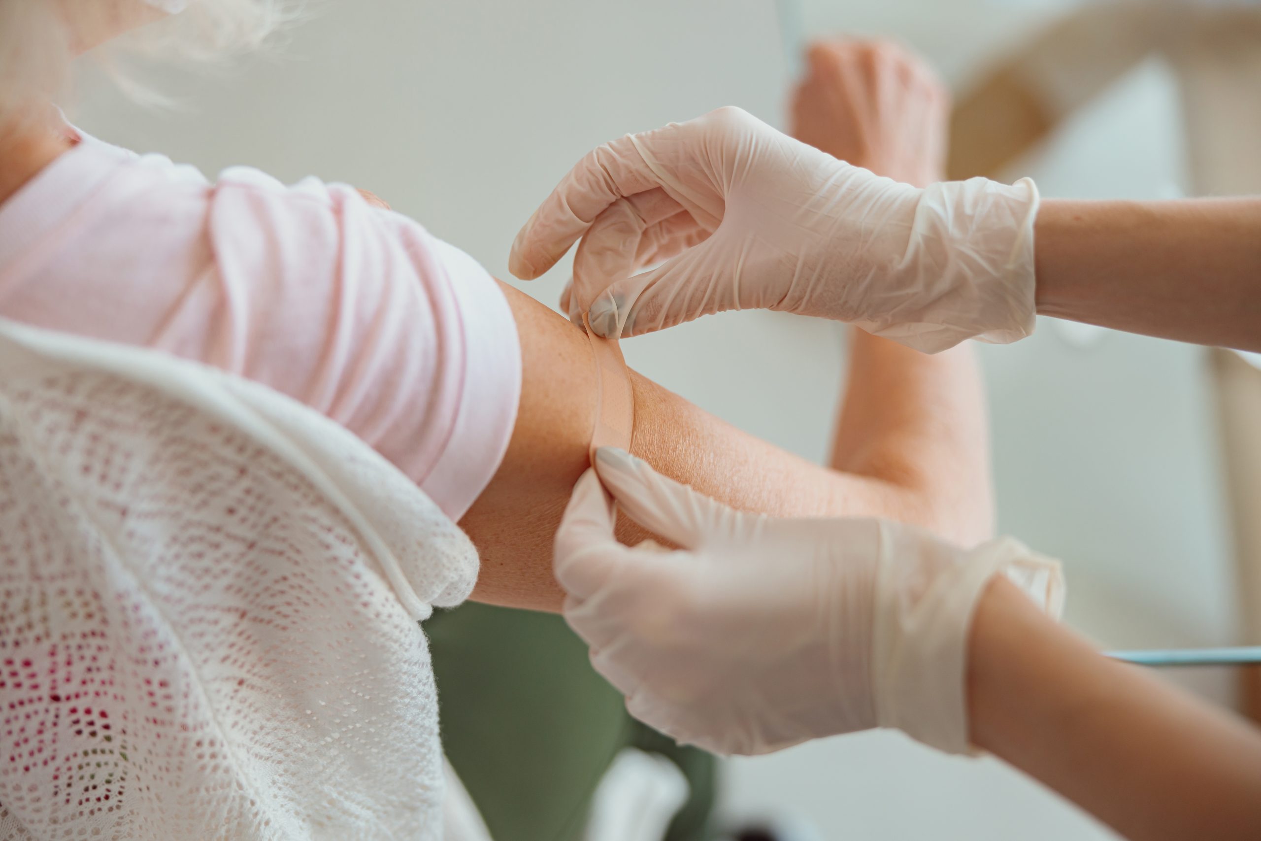 gloved hands applying bandaid to arm after vaccine
