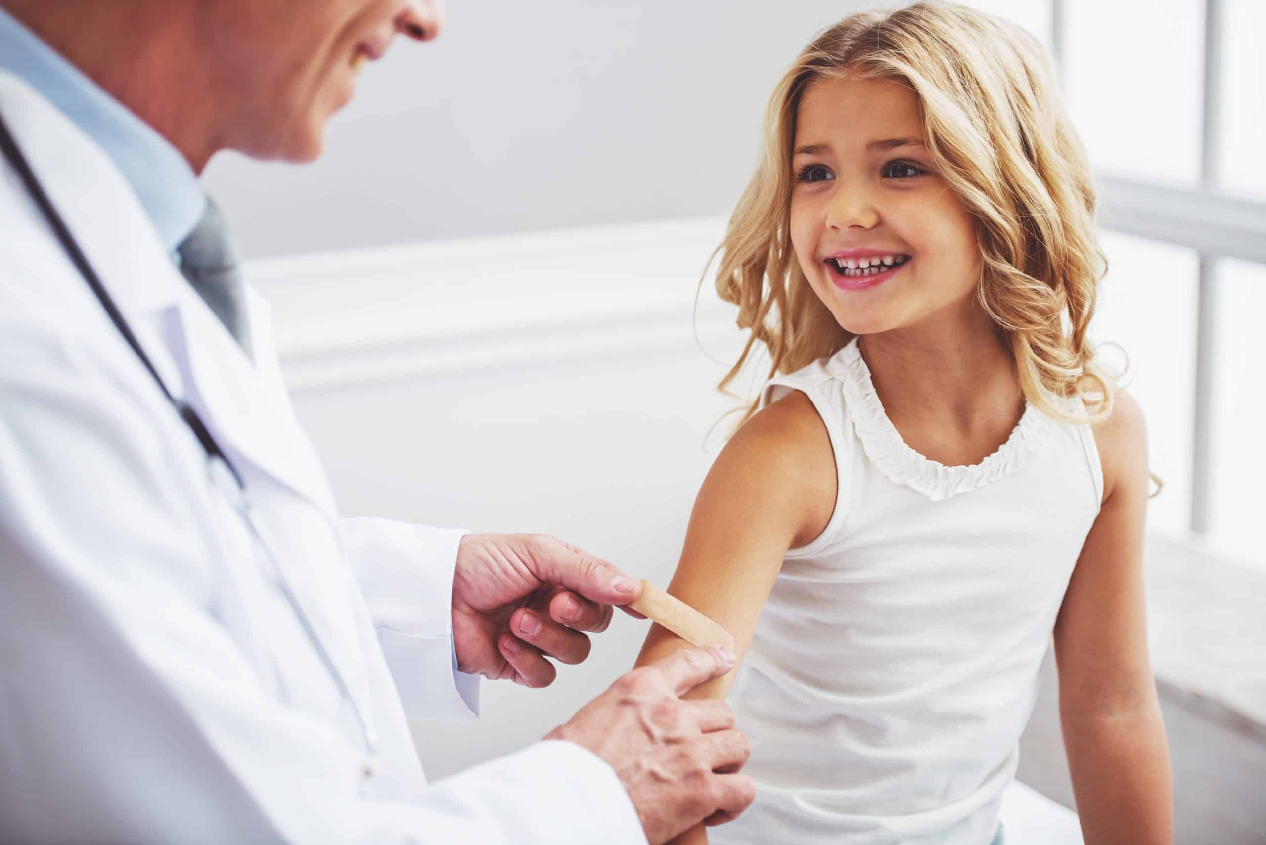 doctor putting bandaid on little girl's arm after vaccine